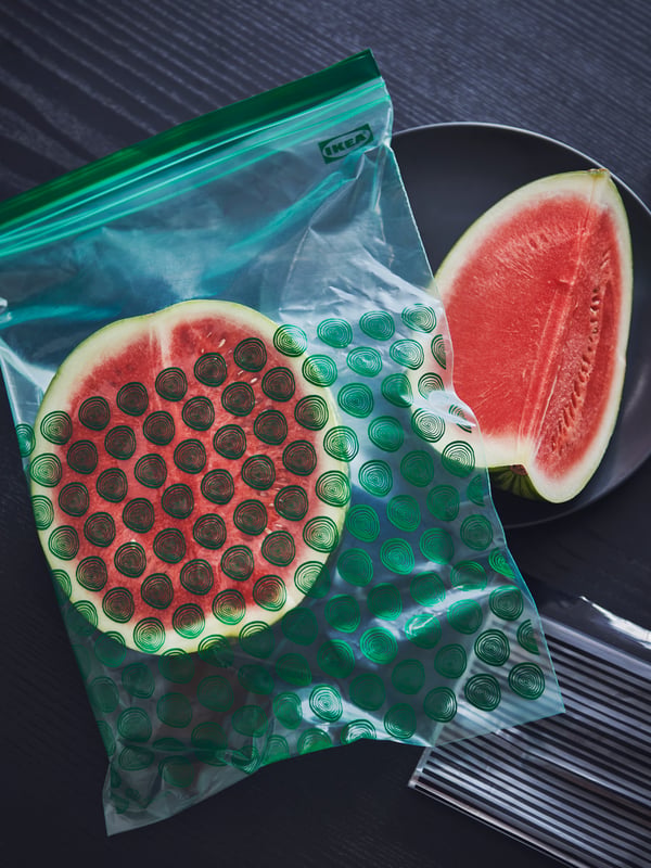 An ISTAD resealable bag containing a piece of a watermelon with another piece of watermelon on a dark plate.