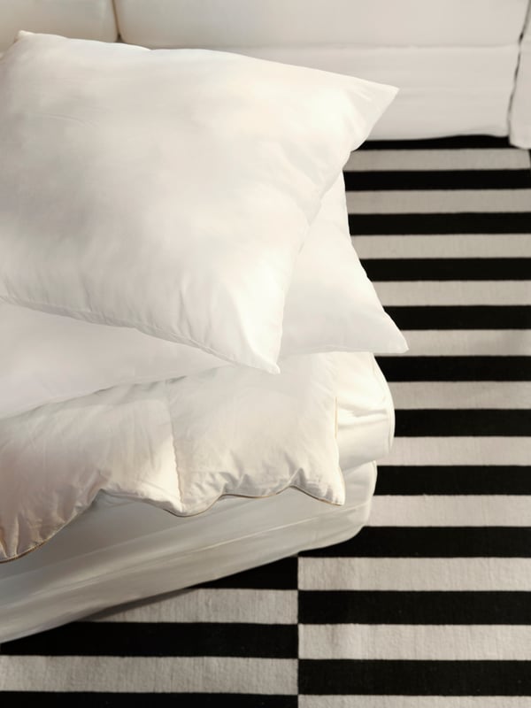 A mattress on top of a black and white STOCKHOLM rug with an uncovered duvet and two LAPPTÅTEL high pillows on top.