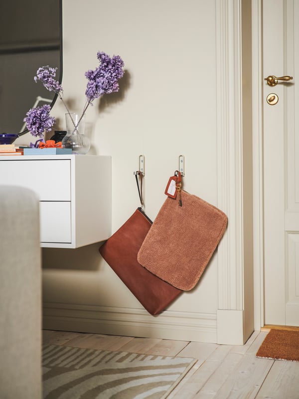 Deux sacs pour ordinateur portable suspendus à des crochets pliables KLYKET fixés sur un mur entre une porte et une armoire EKET à 2 tiroirs.
