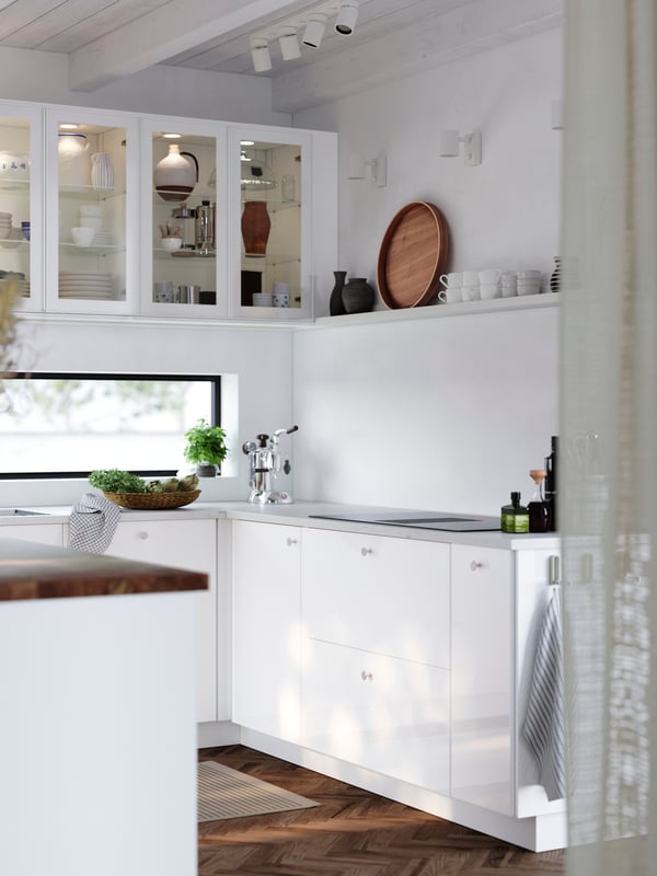 A bright kitchen with glossy RINGHULT fronts and cabinets with HEJSTA glass doors has a kitchen island and a picture ledge.