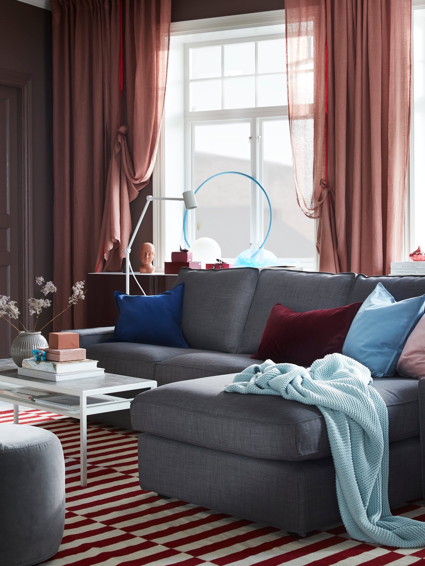 Sofá 3 cuerpos KIVIK color gris con un chaise longue que tiene mantas y cojines encima.