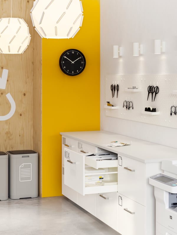 An office with yellow and white walls, white storage with some drawers open, pegboards on the wall with various items.