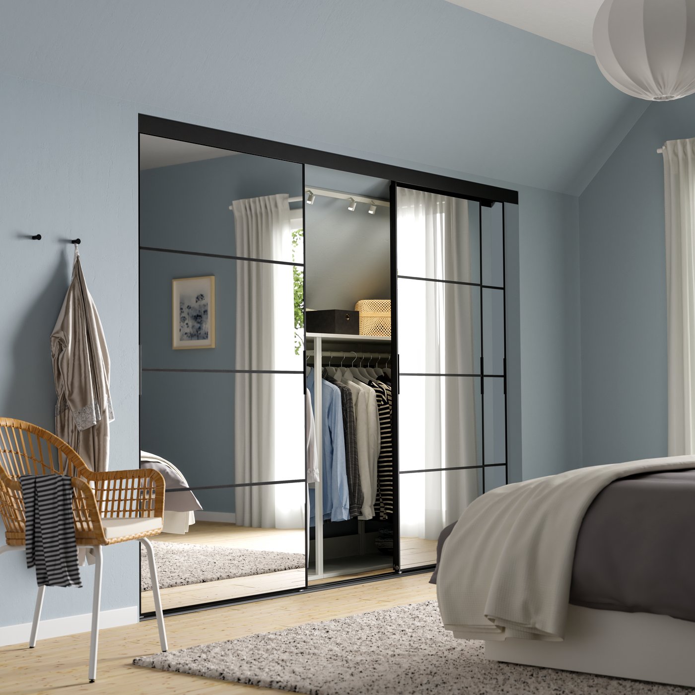 Una habitación ampla con un clóset IKEA PLATSA con puertas de espejo que reflejan el borde de una cama doble y unas cortinas.