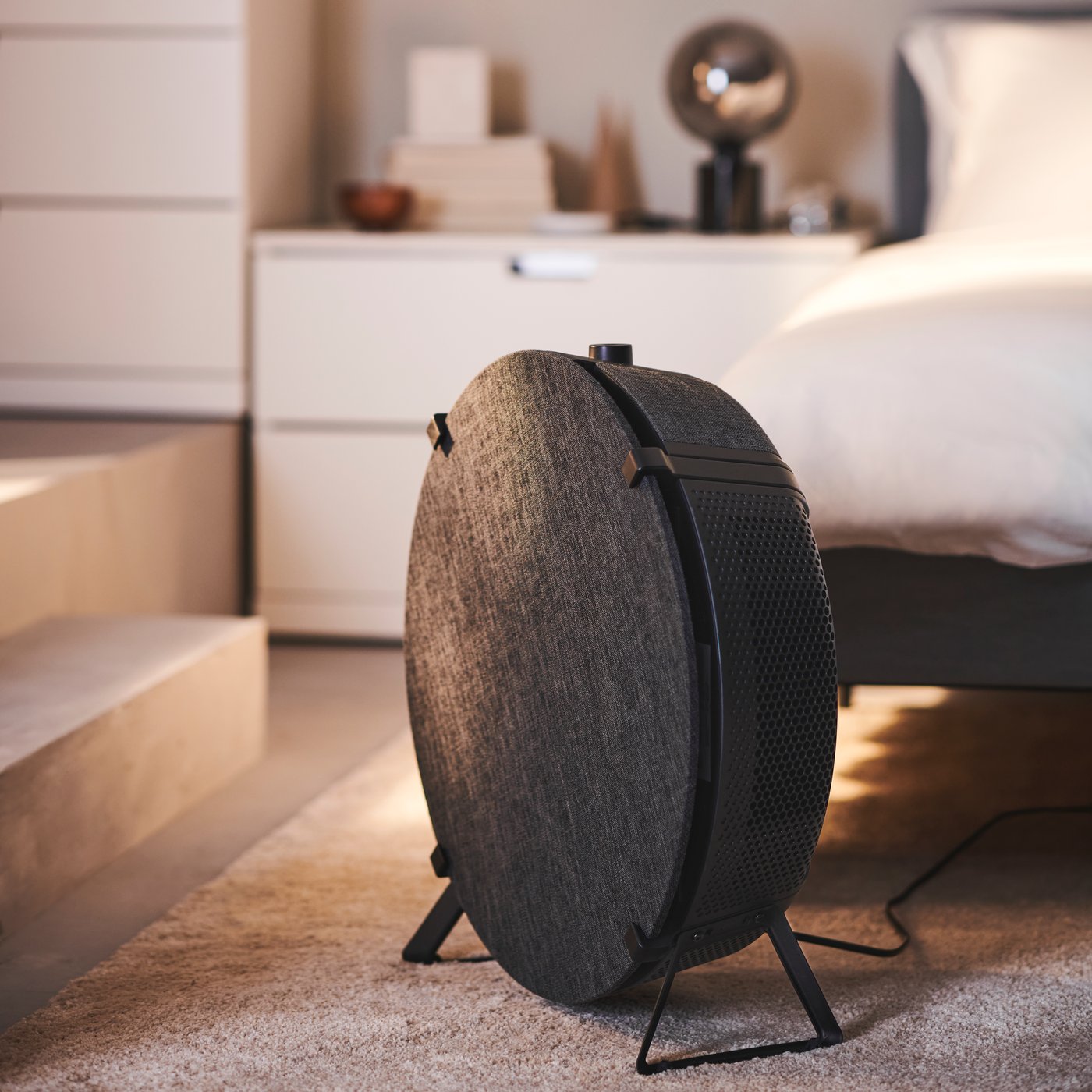 Dark grey STARKVIND smart air purifier in bedroom STOENSE rug infront of chest of drawers and steps.