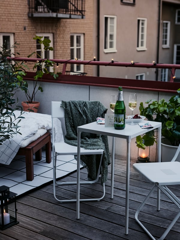 Udobni set za balkon s dve stolice i belim stolom na kom su boca pića i dve napunjene čaše.