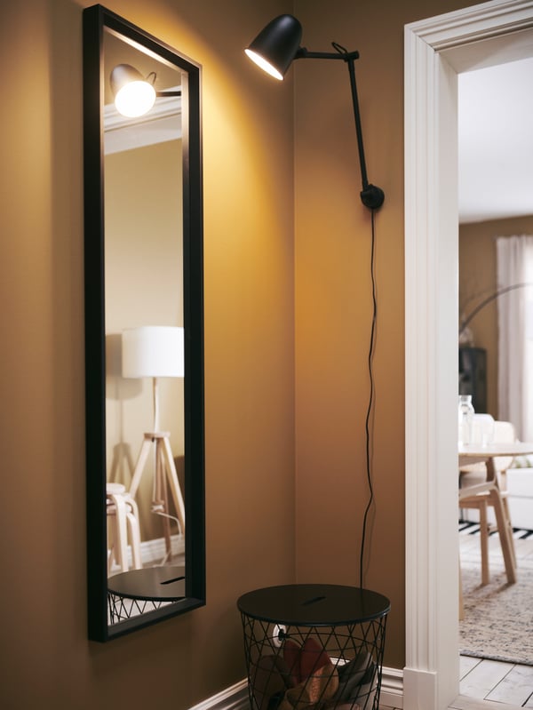 A NISSEDAL mirror in a hallway is illuminated by a SKURUP work/wall lamp on the wall nearby.