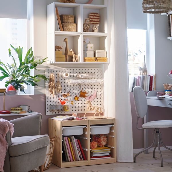 A bright bedroom with an EKET shelf and TROFAST storage against a wall and a SKÅDIS pegboard with art on between them.