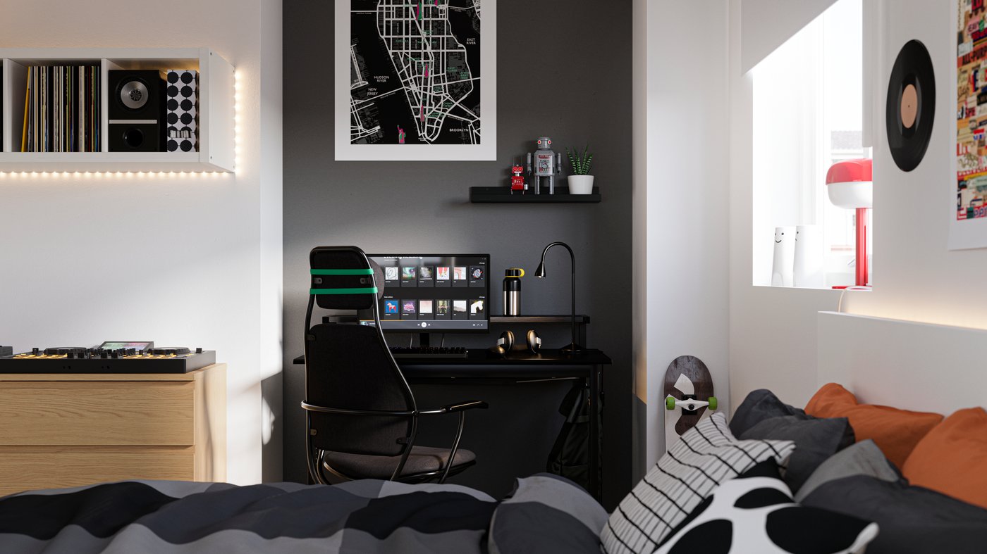 Bedroom with a bed in the foreground and a desk by a wall painted black in the back, with a computer and gaming chair.