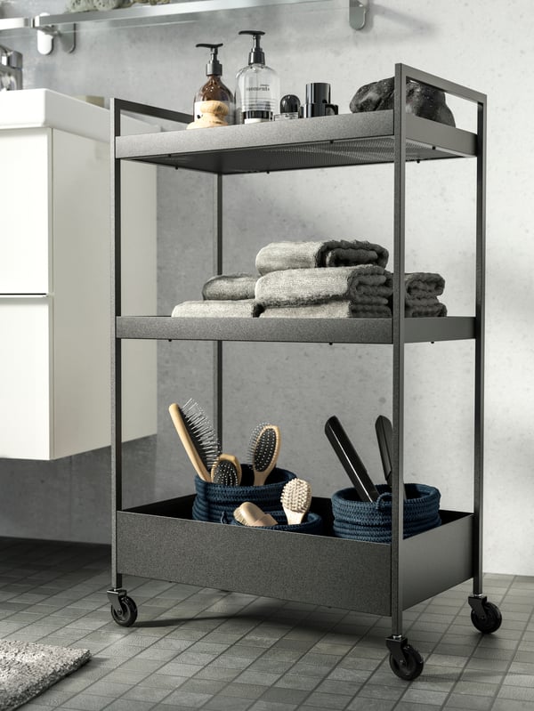 A NISSAFORS black trolley on castors displayed with stylish beauty products, grey towels and hairbrushes in baskets.