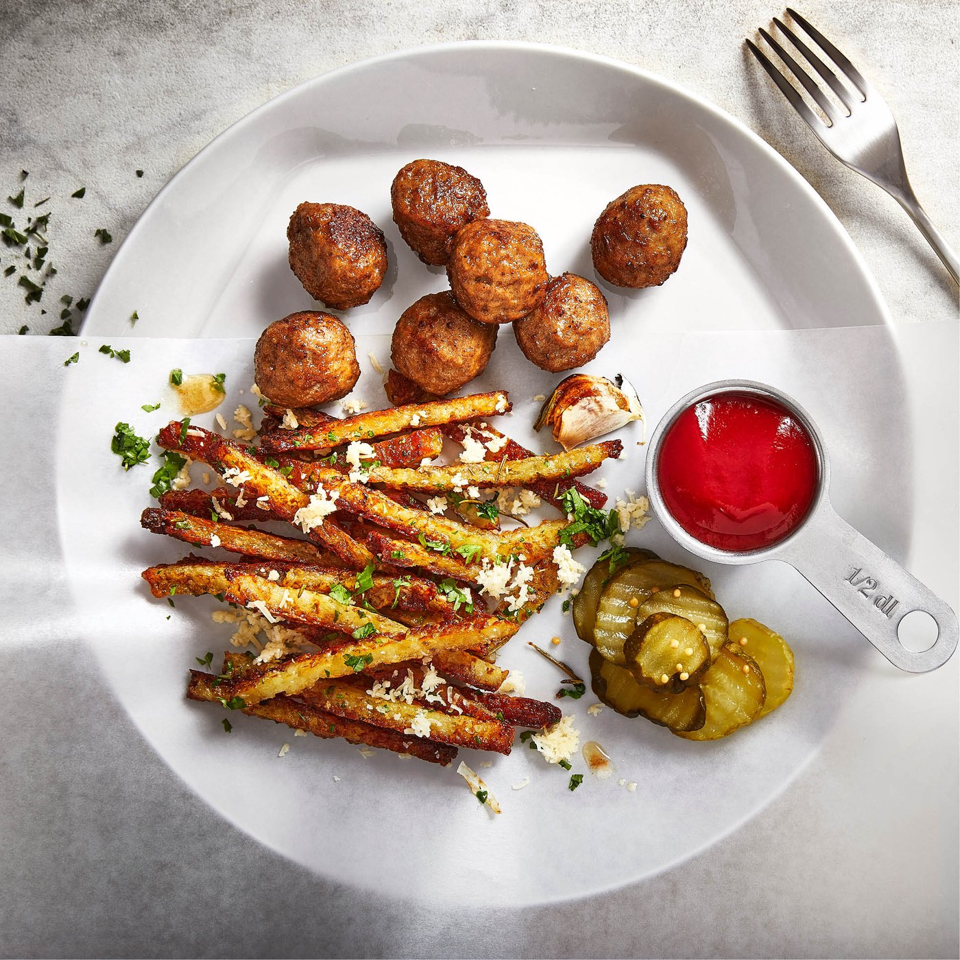 Boulettes de viande avec frites de légumes croustillantes, cornichons et sauce tomate, servies sur une assiette blanche.