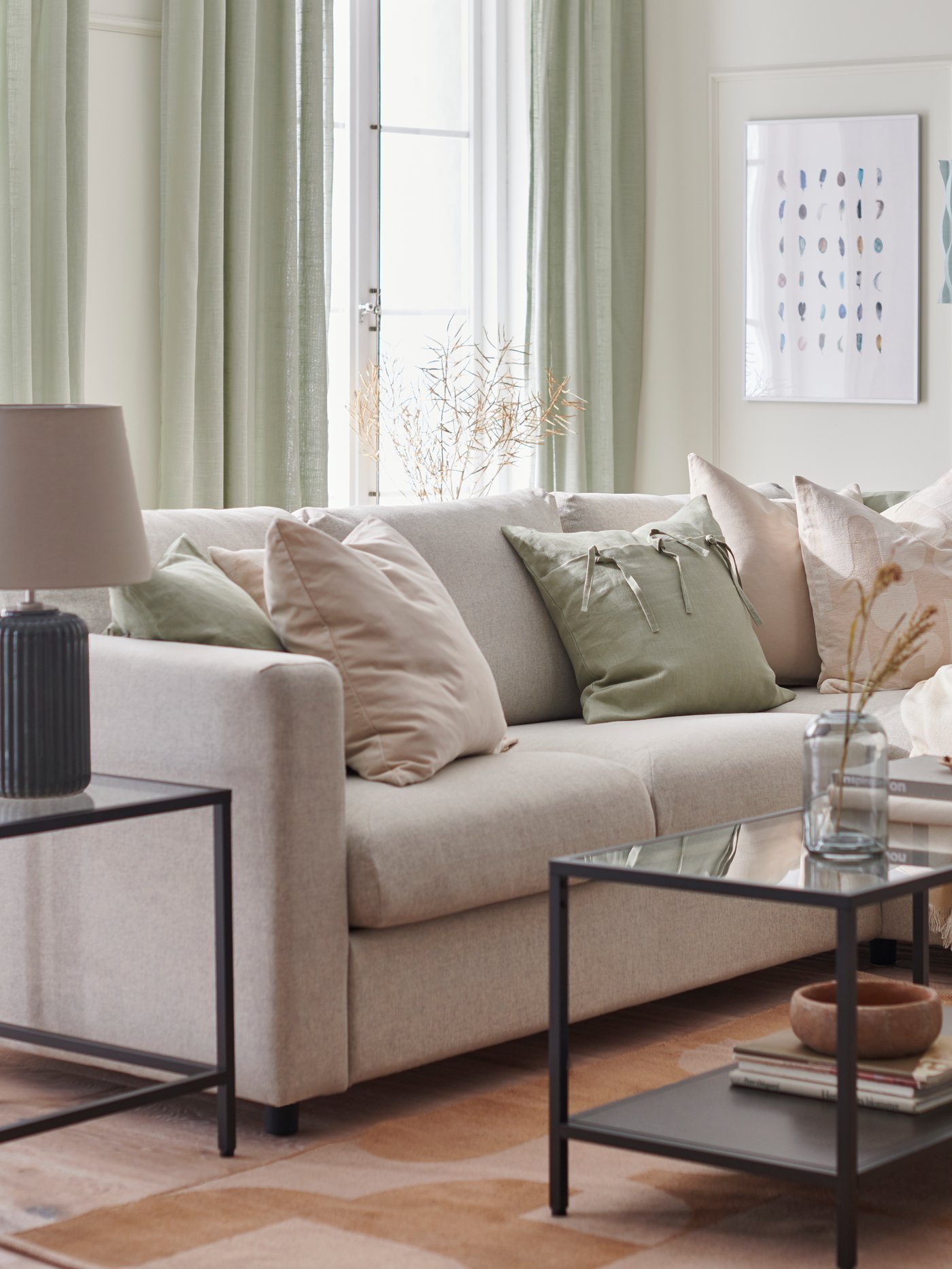 Ein beiges Wohnzimmer mit einem VIMLE-Sofa und RÖDASK-Kissenbezügen. Auf einem VITTSJÖ-Tisch neben dem Sofa steht eine SNÖBYAR-Lampe.