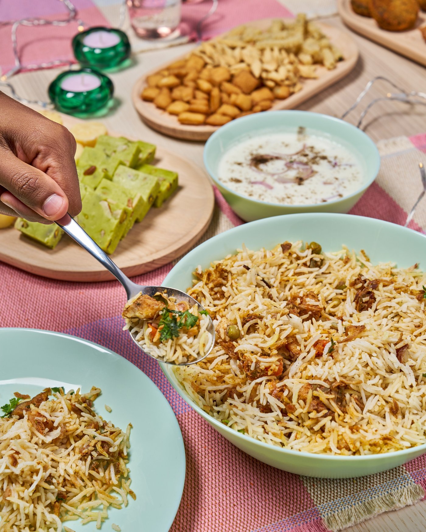 A bowl of steaming biryani with raita and fried onions, served with festive side dishes.