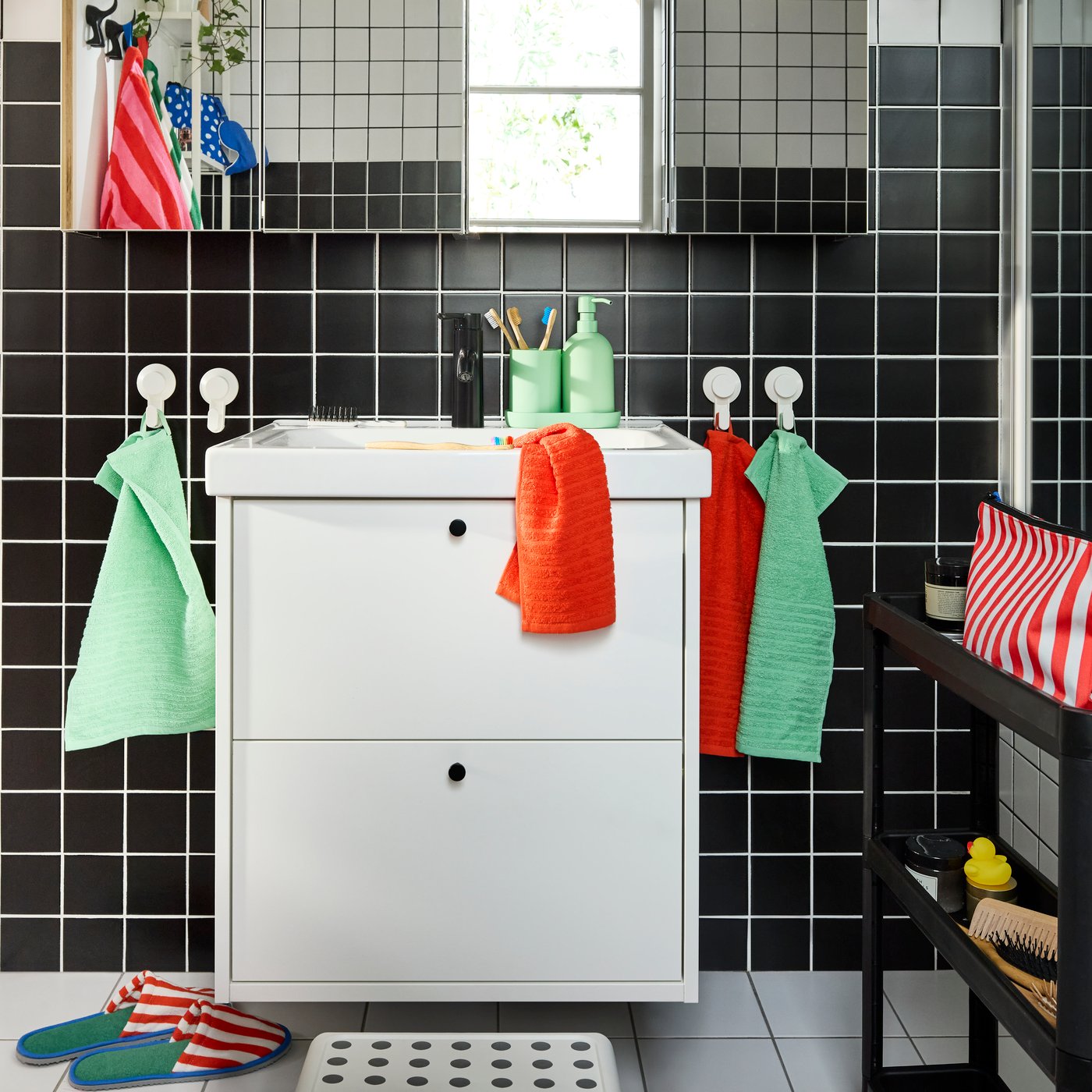 A white HAVBÄCK/ORRSJÖN washstand with two drawers and four mirror cabinets above it. Colourful towels on white hooks.
