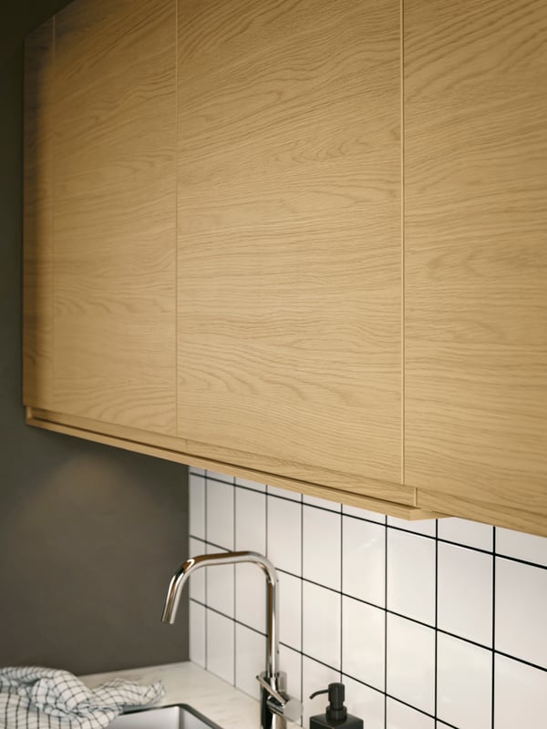 Wall cabinets with VOXTORP fronts with integrated handles and an oak effect are placed above a sink with a kitchen mixer tap.