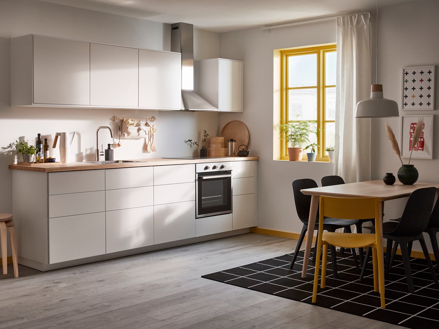 You can see a minimalist kitchen with matte, handle-free fronts and a wooden worktop. In front of the kitchen is a LISABO dining table with four dining chairs.
