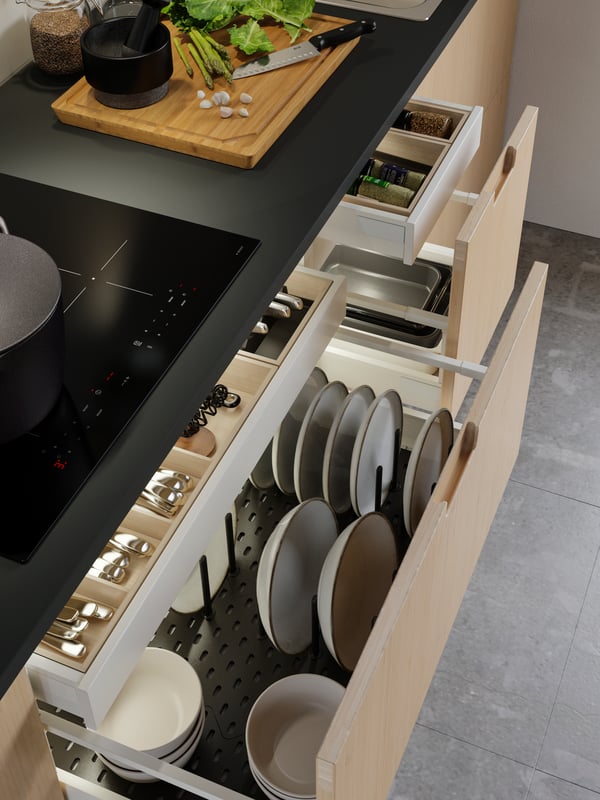 MAXIMERA drawers containing tableware and kitchenware are pulled out from cabinets under a kitchen worktop and a hob.