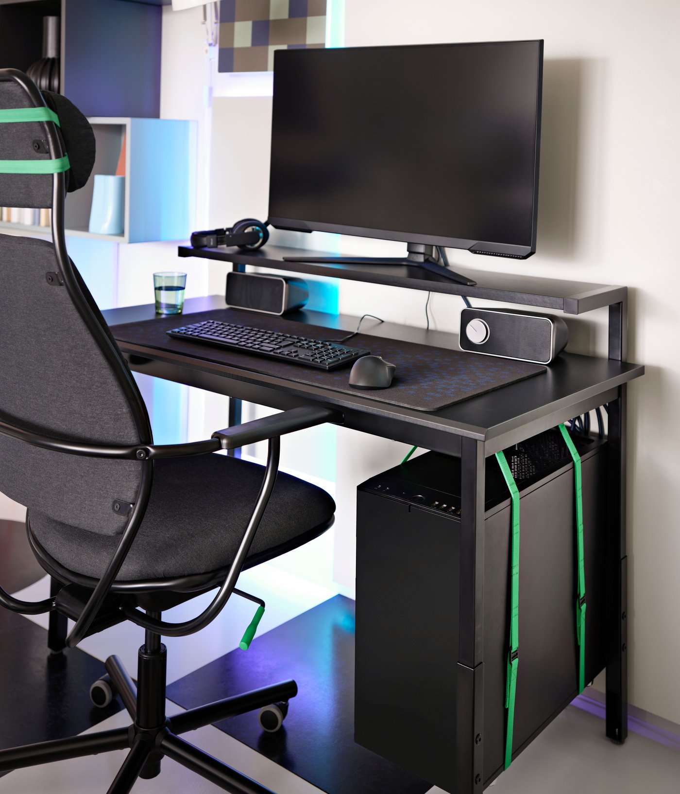 A black UTVSNING gaming desk with shelf has a monitor, keyboard, mouse, etc. on it and a CPU held below using green straps.