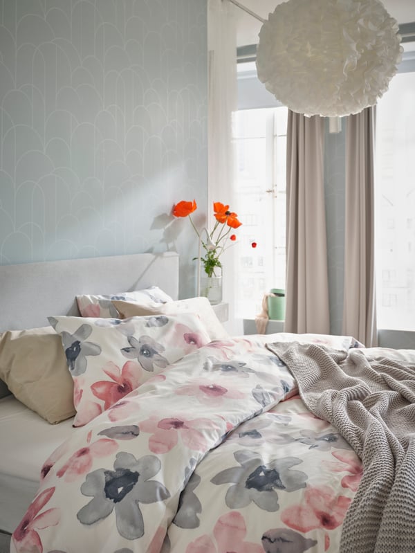 Letto GLADSTAD con biancheria da letto fantasia floreale rosa e grigio e un vaso con dei papaveri sul comodino accanto al letto - IKEA