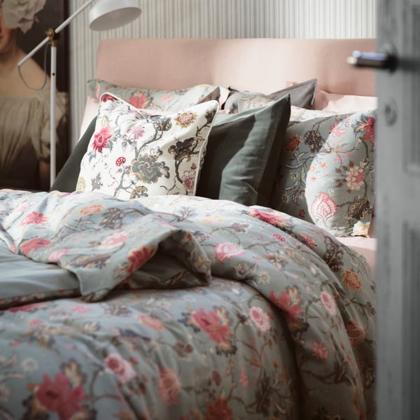Un lit fait avec une housse de couette rose et vert clair à motifs fleuris et des oreillers assortis.