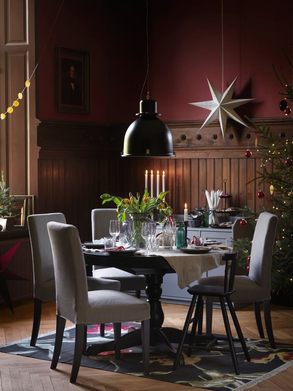 A round black INGATORP table set for a festive meal. A SVARTNORA pendant lamp is over the table and a star is behind it.