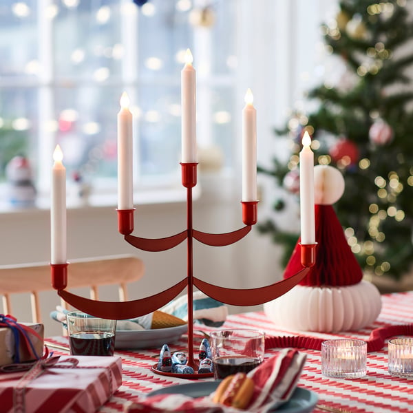 Röd adventsljusstake med fyra tända ljus på dukat bord.