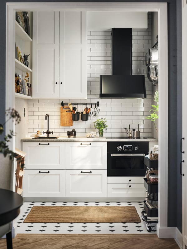 A kitchen with matte white AXSTAD fronts features two base cabinets, a tall wall cabinet, black appliances and a brown rug.