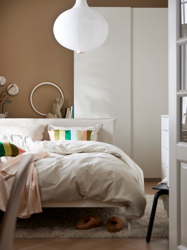 A KLEPPSTAD bed with ÄNGSLILJA bed linen stands in front of a white PAX/HASVIK wardrobe with sliding doors.