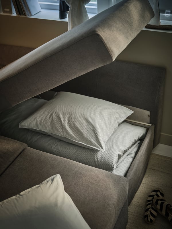 Krupni plan jastučića sofa ležaja koji je podignut kako bi se pokazao prostor za odlaganje dodatnih jorgana i jastuka.