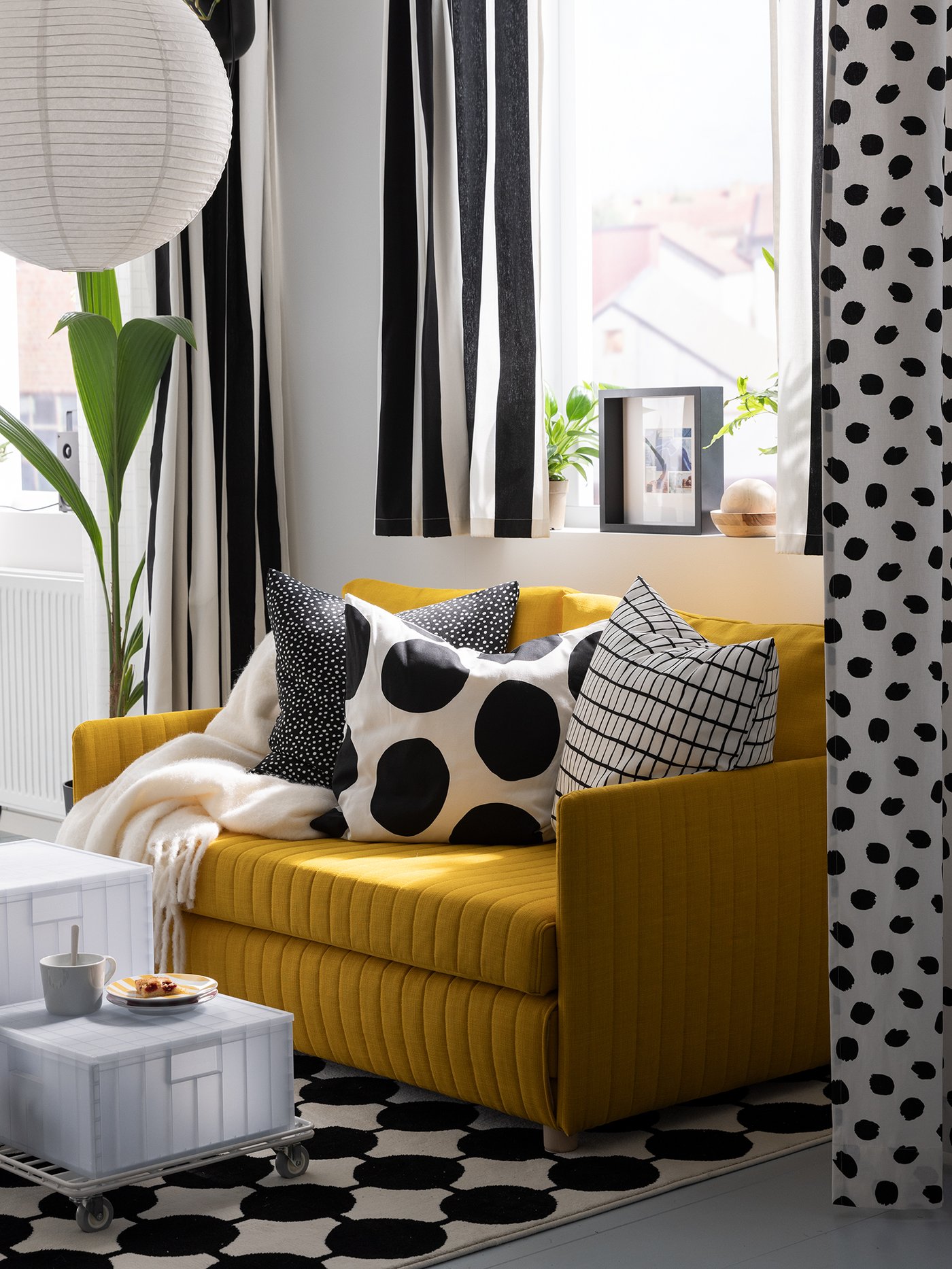 Curtains made from striped black and white VARGTÖREL pre-cut fabric hang in a room near a yellow FRIDHULT sofa-bed.
