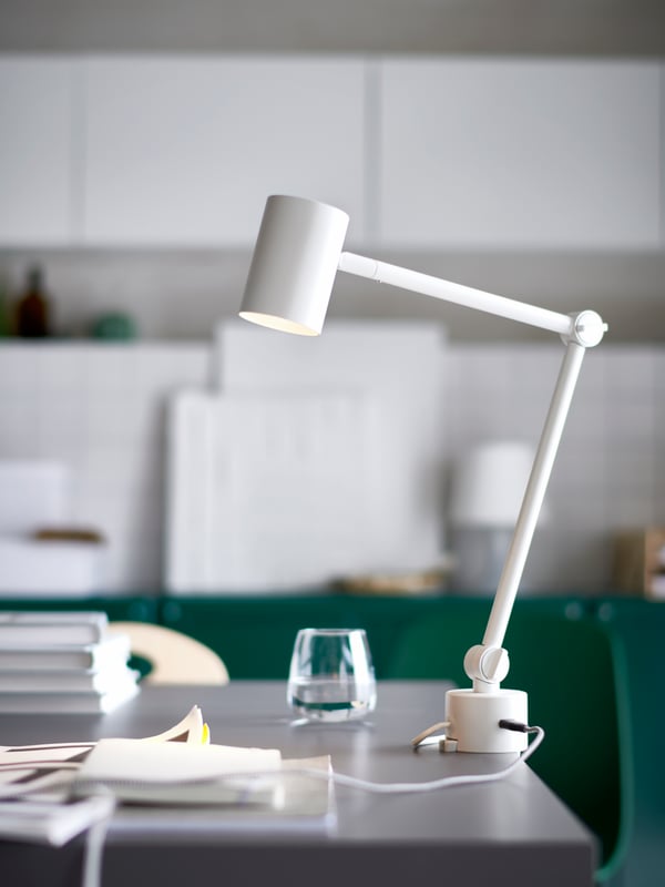 Lampu kerja/dinding NYMÅNE berwarna putih dengan kabel yang disambungkan ke port USB dikapit pada meja LAGKAPTEN/KRILLE berwarna kelabu gelap/putih.