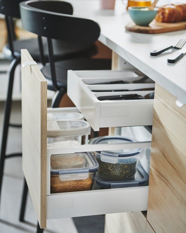 Des éléments IKEA METOD habillés de façades lisses ASKERSUND effet frêne avec deux tiroirs ouverts servant à conserver les produits alimentaires secs.