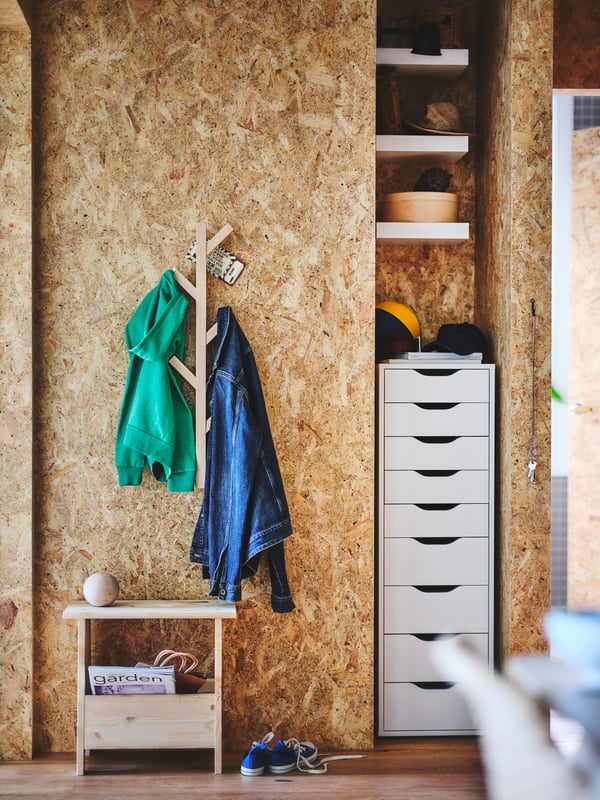 An ALEX drawer unit sits below three LACK shelves in a hallway alcove. A TJUSIG hook rack is hanging on the wall nearby.