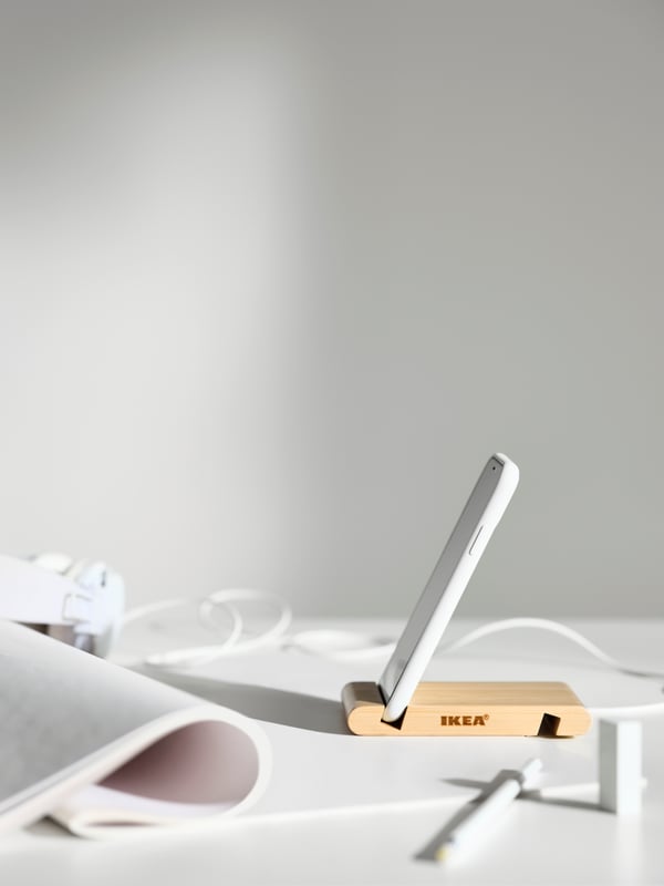 A mobile phone in a BERGENES holder for mobile phone/tablet on a white table, near a rolled-up document and headphones.
