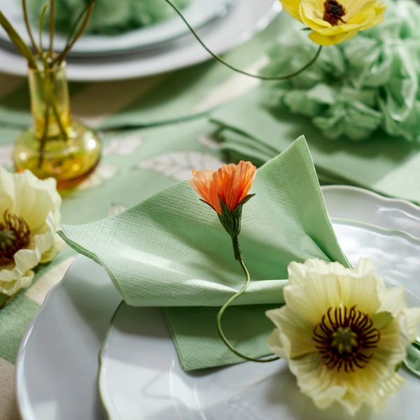 Serviette en papier vert clair sur une assiette et une petite assiette blanches, décorées de fleurs artificielles.