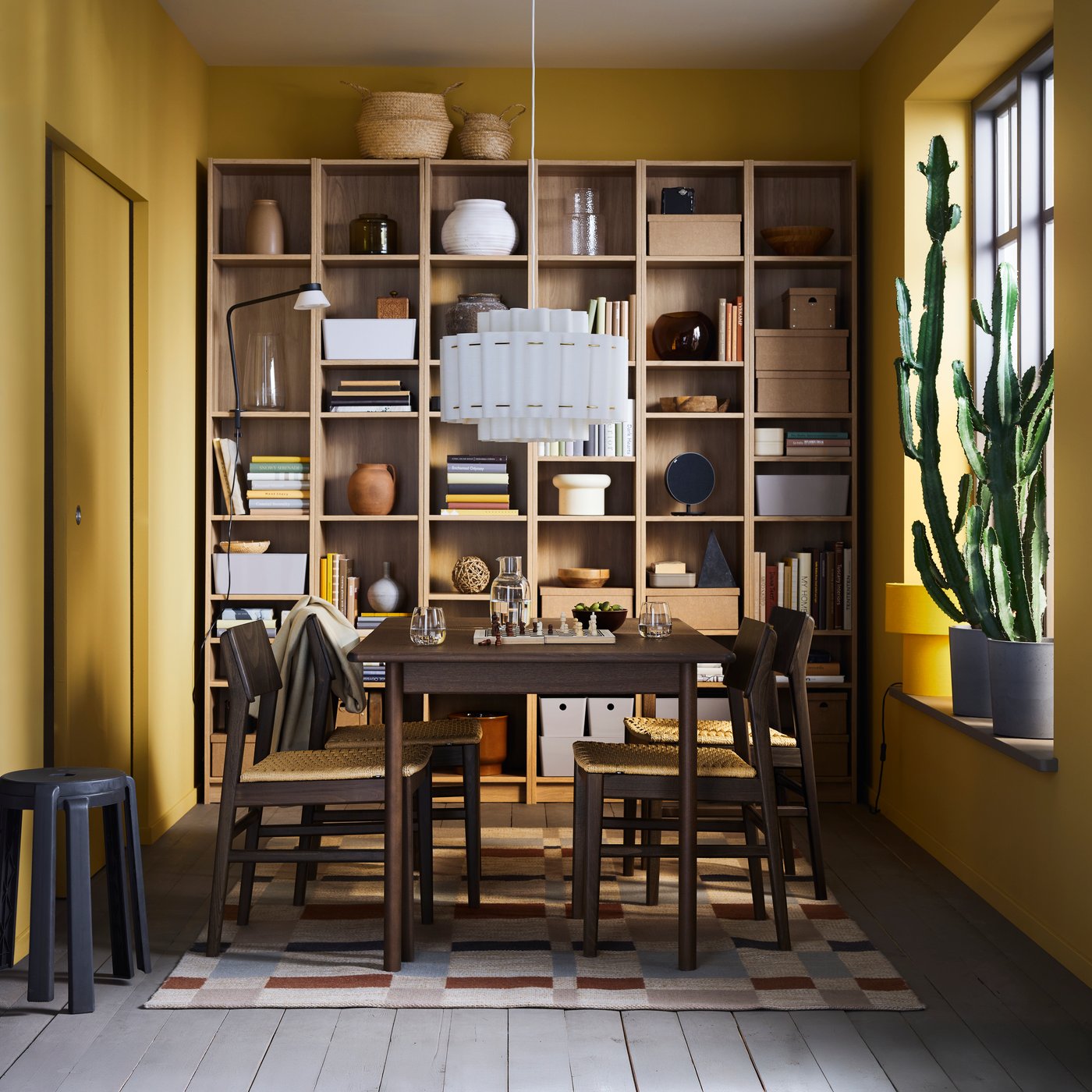 A dining area with yellow walls features a SKANSNÄS extendable table and BILLY bookcases with books, vases and decorations.