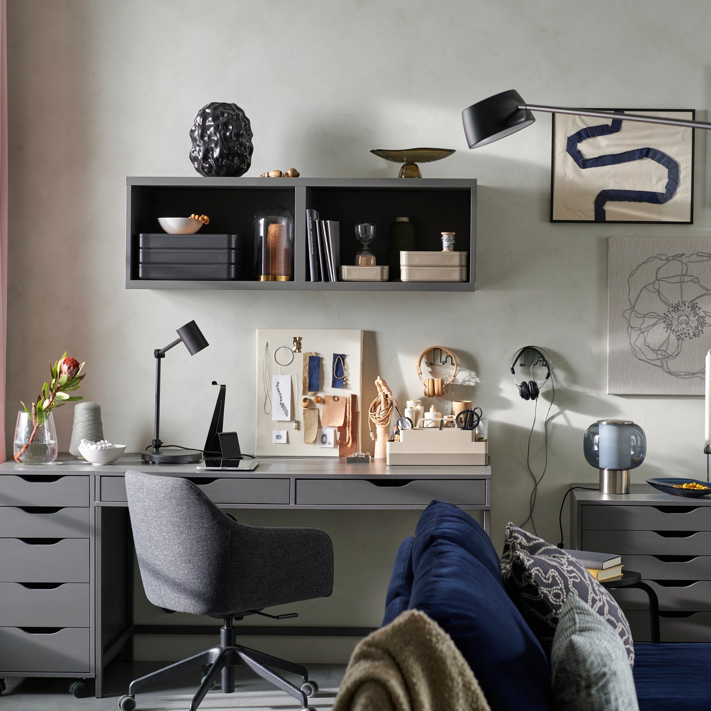 A living room with a sofa, art wall, and a hobby area created with the ALEX series of dark grey desk and storage units.