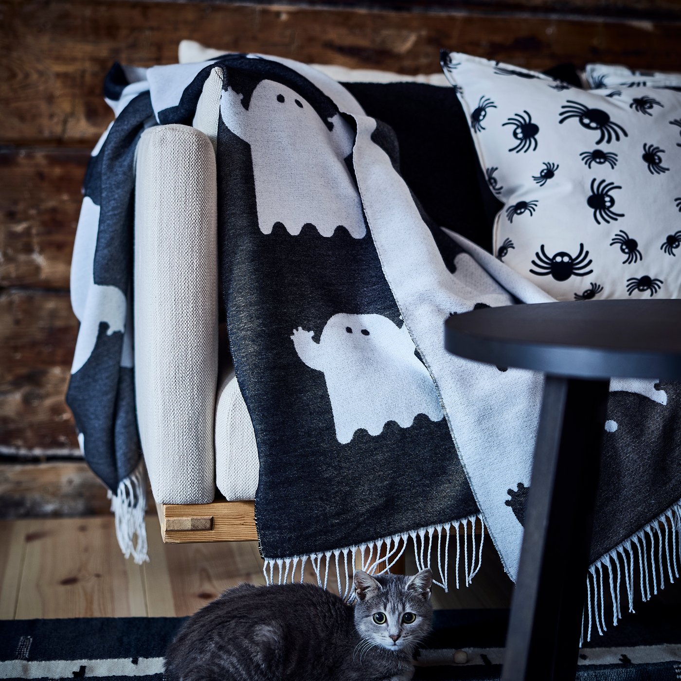 A black‑and‑white KUSTFYR throw with little ghosts draped over a sofa in the living room.