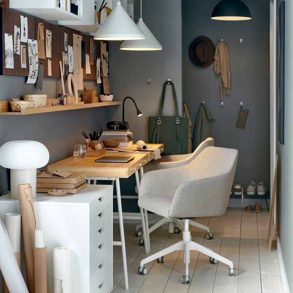 A workspace in a narrow space with grey walls, drawings pinned on pegboards and a TOSSBERG/LÅNGFJÄLL conference chair.