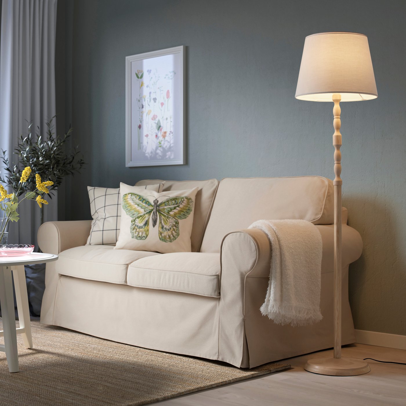 An ash/white KINNAHULT floor lamp next to a beige sofa in a living room