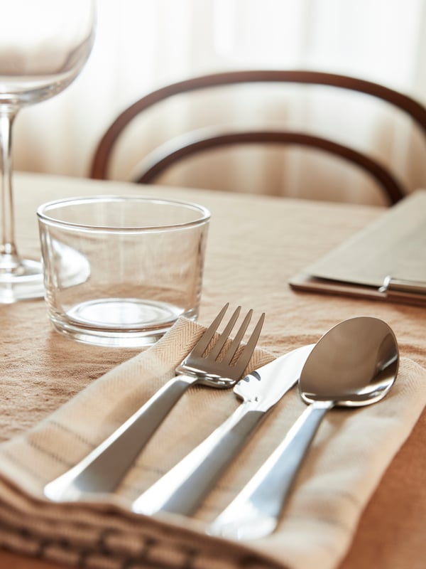 A clear glass IKEA 365+ glass in the dining room next to DRAGON cutlery.