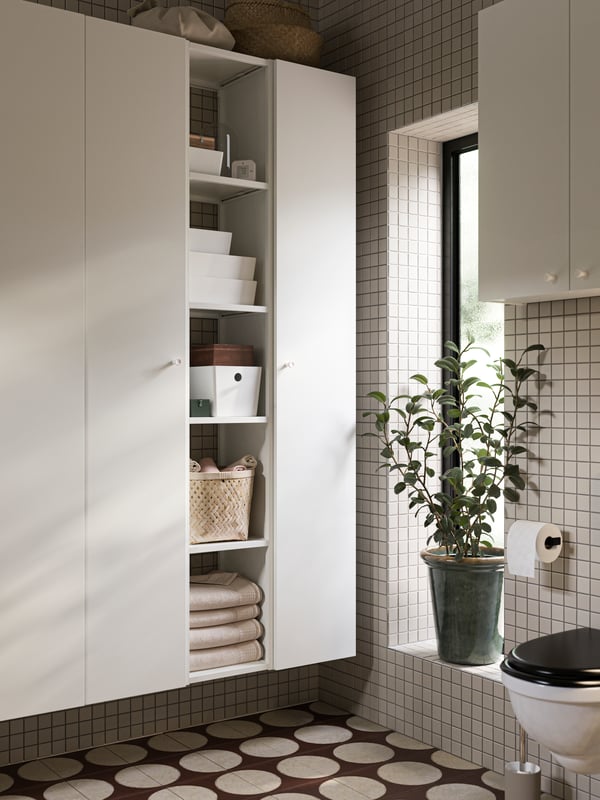 A bathroom with ENHET high cabinets with four shelves and ENHET doors in white and KUGGIS boxes with lids in white.
