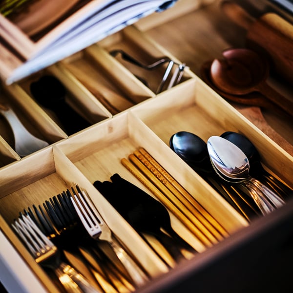 An open drawer revealing an UPPDATERA cutlery tray filled with cutlery including forks, wooden chopsticks and spoons.