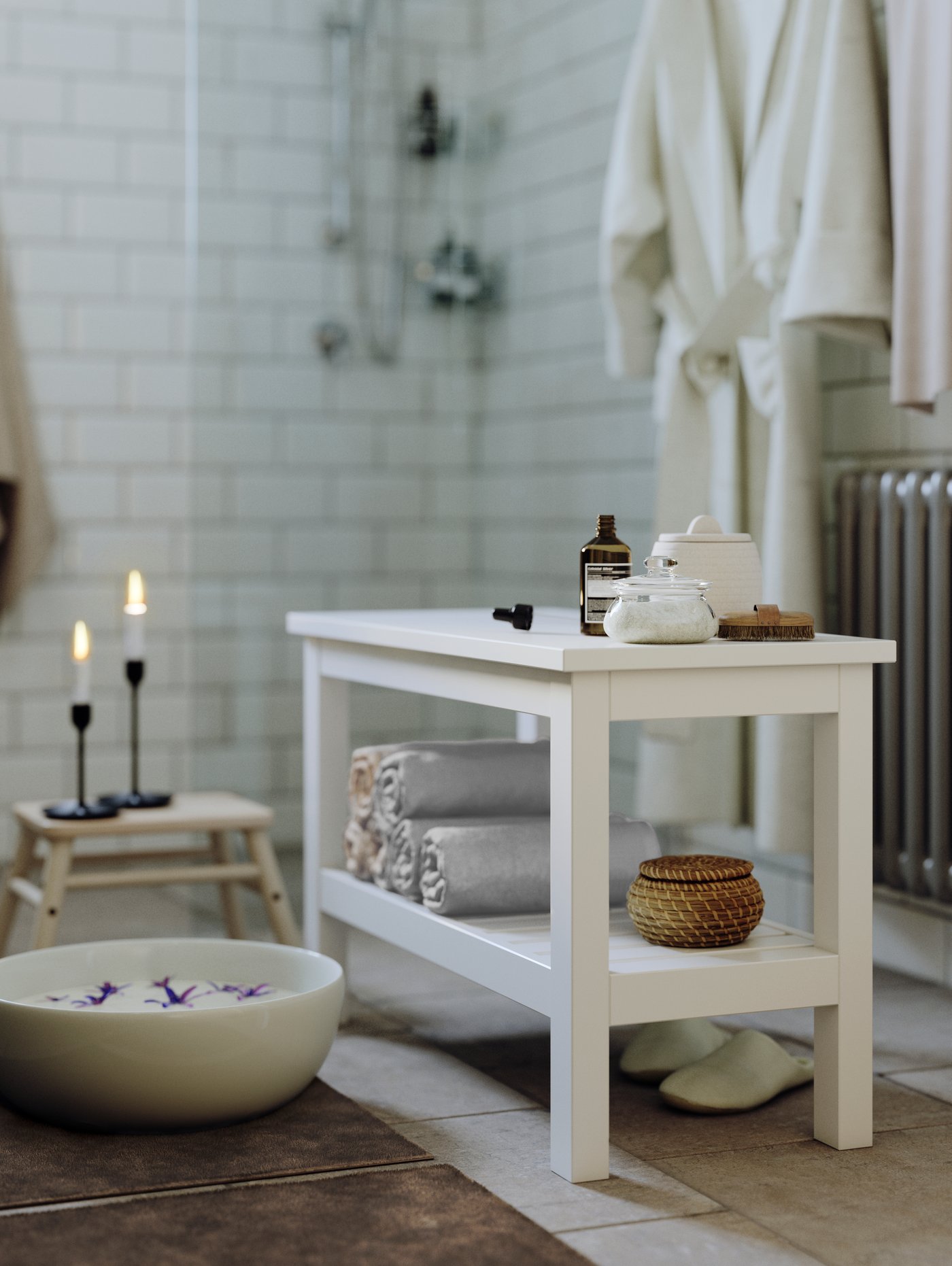 Et badeværelser med spastemning - der står en hvid HEMNES bænk med spaprodukter på, og på en skammel ved siden af står to tændte stearinlys.