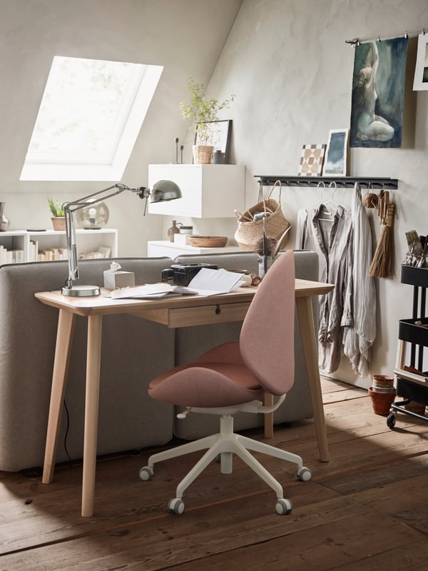 A LISABO desk in ash veneer behind a sofa, a FORSÅ work lamp and the back of a GUNNARED swivel chair.
