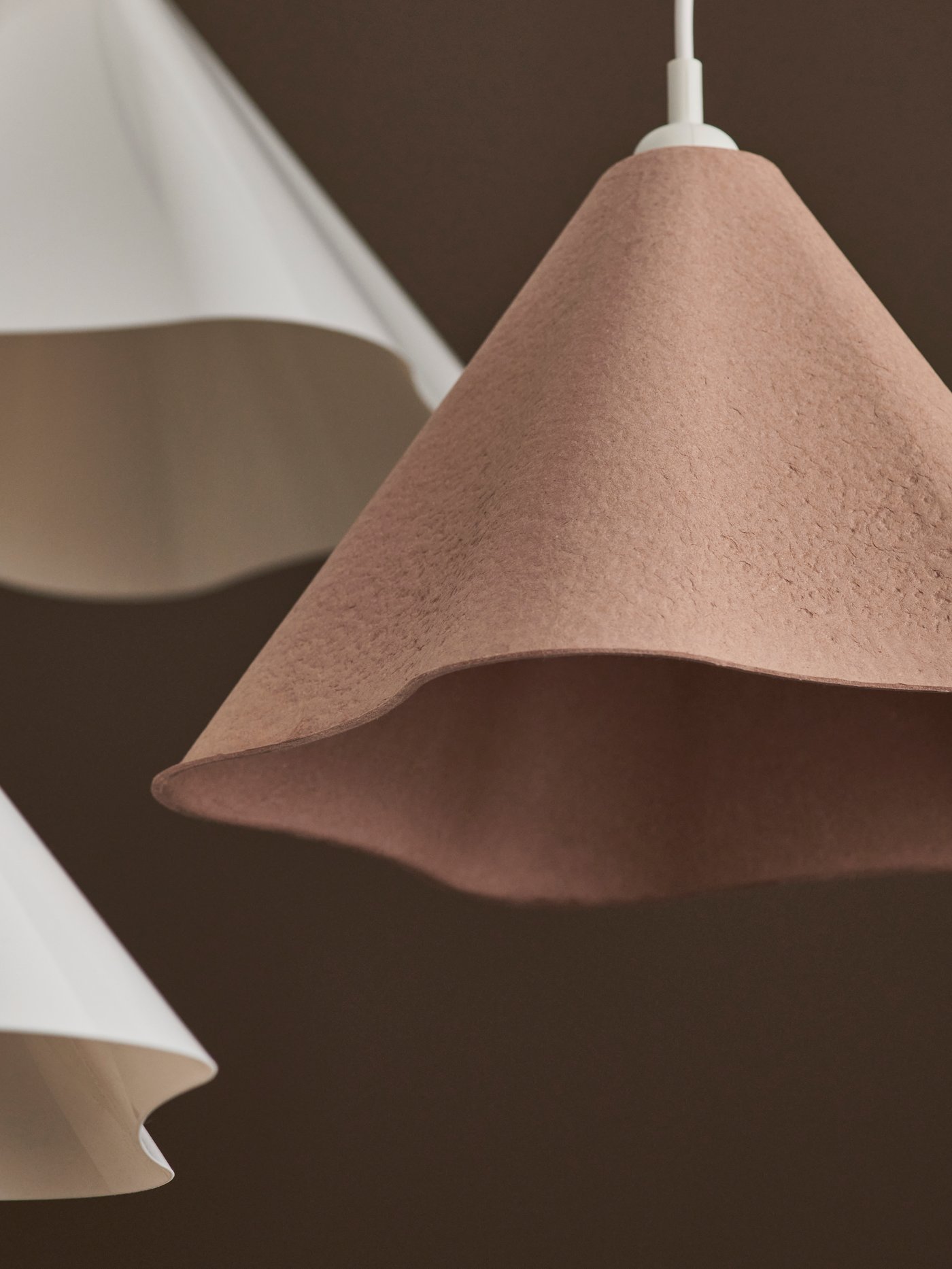 Close up of a beige ZEBRSÄV pendant lamp with two white ones out of focus behind it.