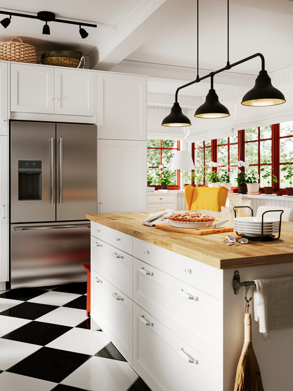 Una cocina grande con una isla de cocina con mesón de madera. Sobre la isla una lámpara de techo AGUNNARYD con sus 3 luces encendidas.
