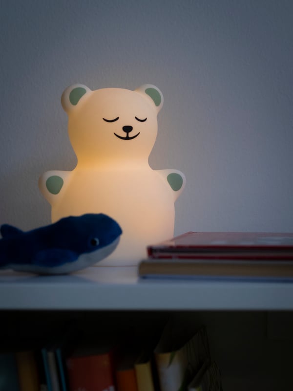 TÖVÄDER led-nachtlampje in de vorm van een beertje staat op een open kast met twee boeken en een walvisknuffel.