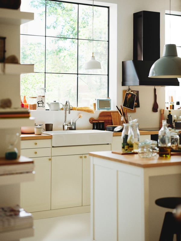 A kitchen with a kitchen island and an off/white RANARP pendant lamp above a worktop with off-white BODBYN doors below.