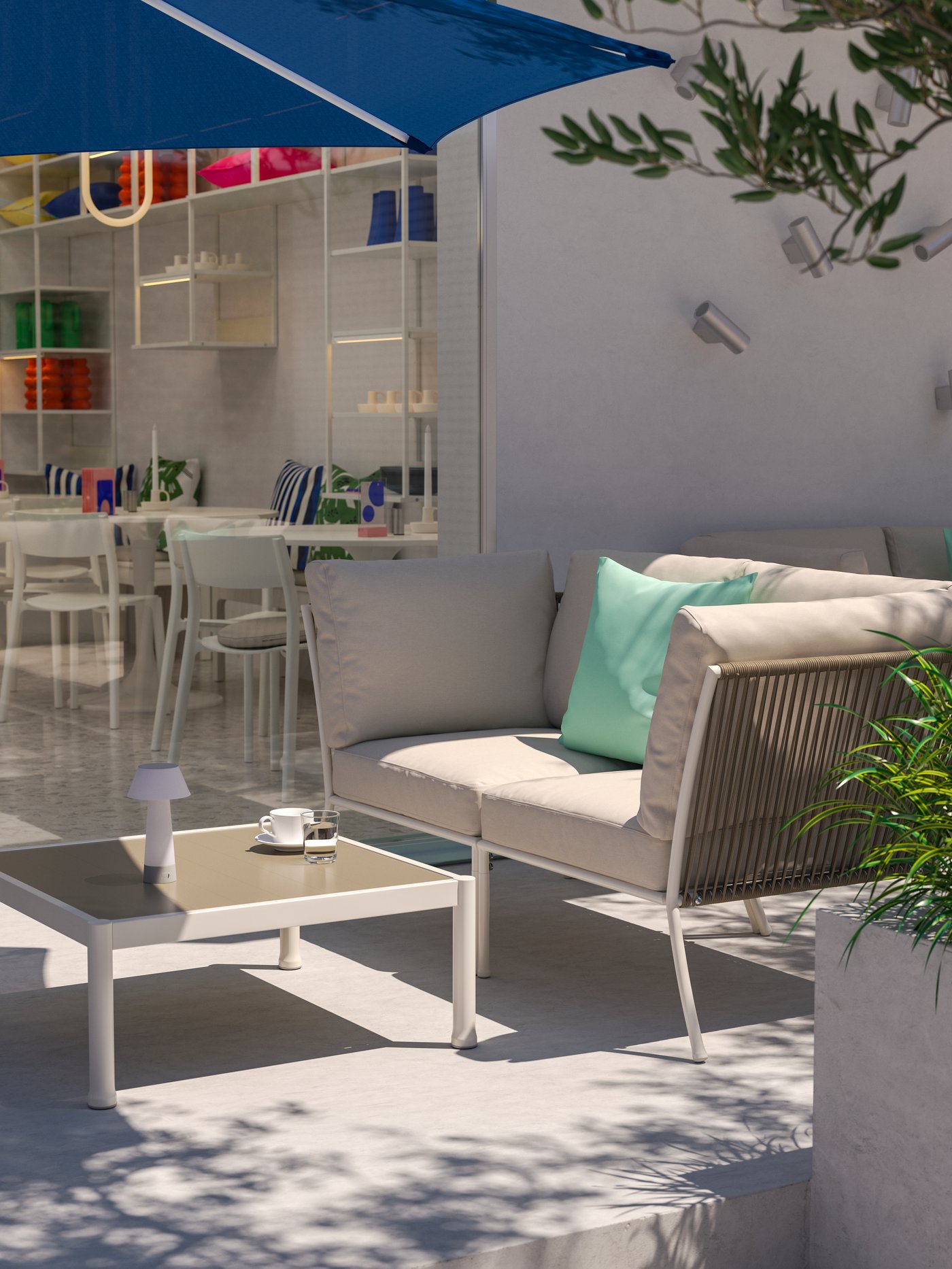 Una soleggiata area lounge di un bar all'aperto con un set di mobili da giardino a 5 posti SEGERÖN bianco/beige, un ombrellone blu e alcune piante.