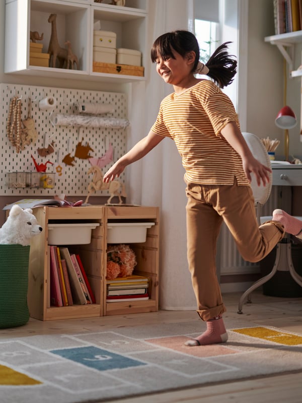 Unaniña juega en su habitación y al costado de ella se ve un mueble para organizar juguetes TROFAST.